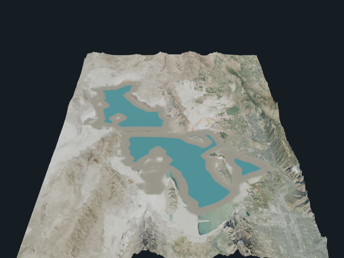 Three-dimensional terrain model of the Great Salt Lake basin viewed from the south: two blue lake lobes split by the railroad causeway, ringed by a wide band of pale exposed lakebed, with the Wasatch Range rising along the eastern edge.